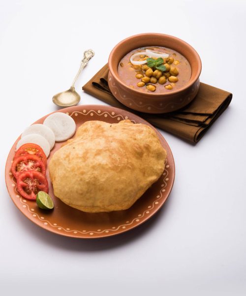 Chole Bhature or Chick pea curry and Fried Puri served in terracotta crockery over white background. selective focus