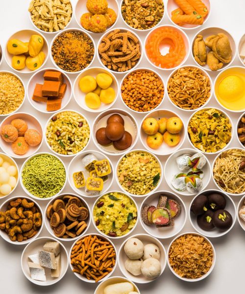 Rangoli of sweets and Farsan or snacks in bowls for Diwali with diya over white background